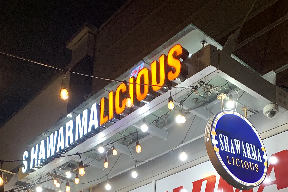 Shawarmalicious sign and round badge lit up at night on 17th Ave SW