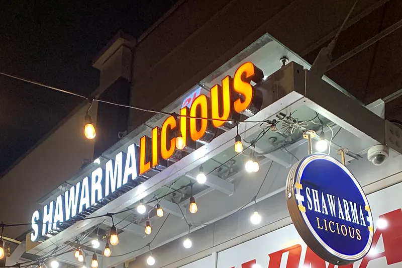 Shawarmalicious sign and round badge lit up at night on 17th Ave SW