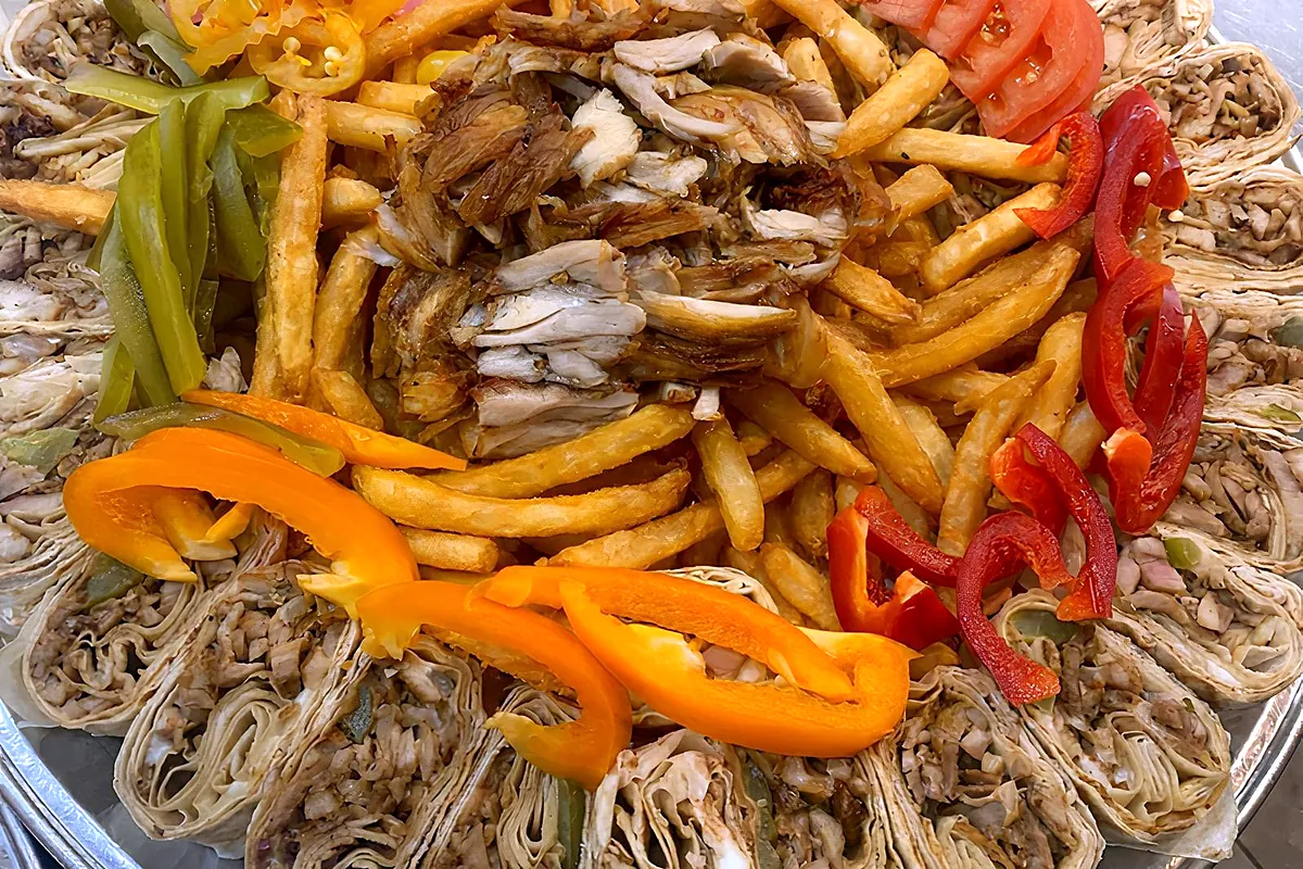 Platter of sliced shawarma wrap bites around fries, peppers and pickles