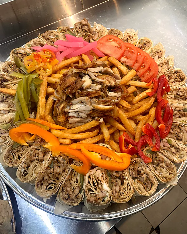 Platter of sliced shawarma wrap bites around fries, peppers and pickles