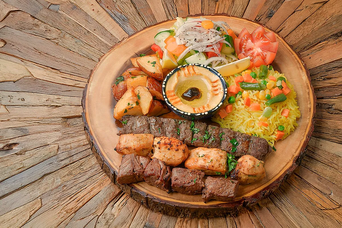 Trio BBQ platter of kabab and tawook skewers on a wooden board with rice and hummus