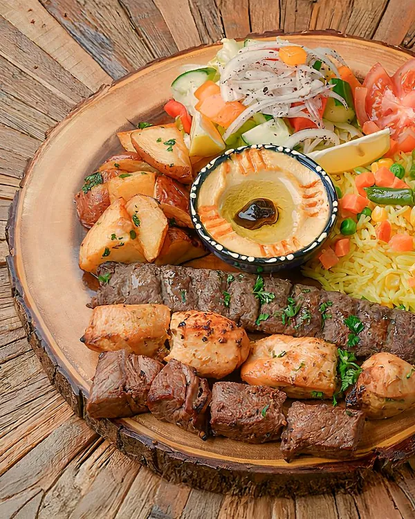 Trio BBQ platter of kabab and tawook skewers on a wooden board with rice and hummus