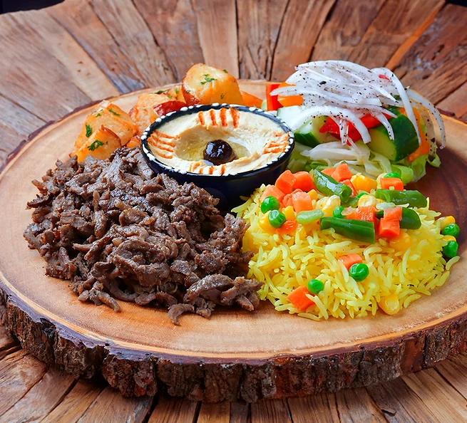 Beef shawarma platter with rice, hummus and salad on a wooden board